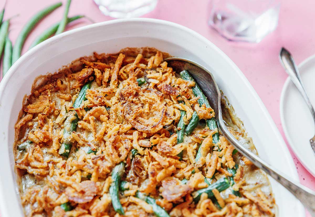 A metal spoon dipped into a casserole dish filled with vegan green bean casserole