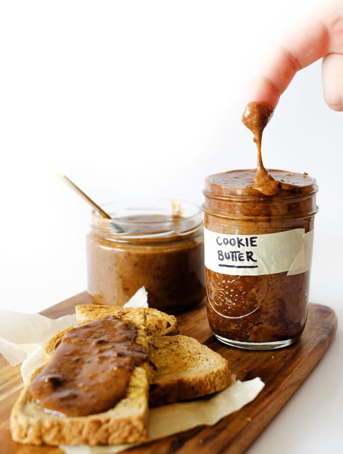 Dipping finger in a jar of cookie butter on white background