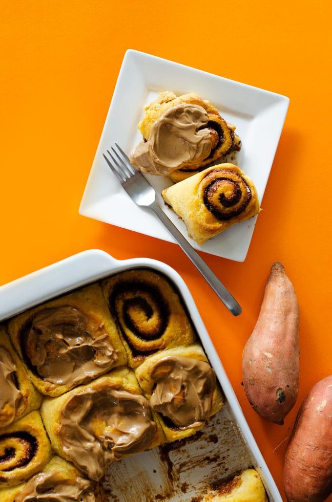 Sweet potato cinnamon rolls on a plate with frosting on an orange background.