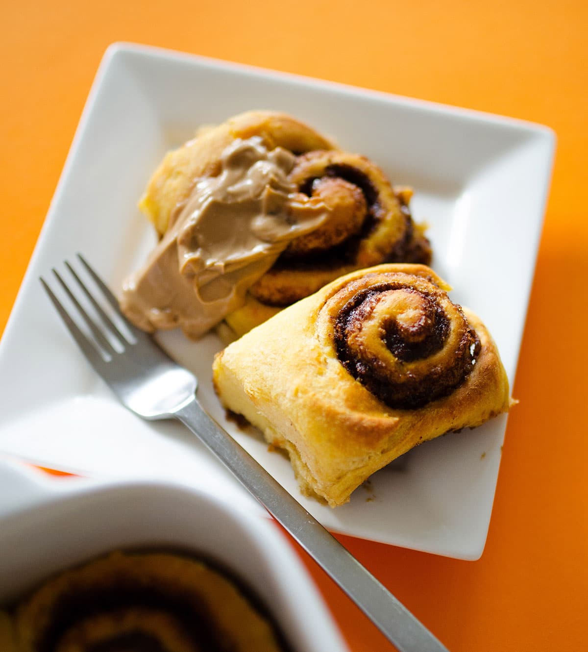 Cinnamon rolls on a plate with a fork - Fluffy, decadent, in slathered in a simple brown sugar cream cheese frosting, these Sweet Potato Cinnamon Rolls are the perfect way to wake up.
