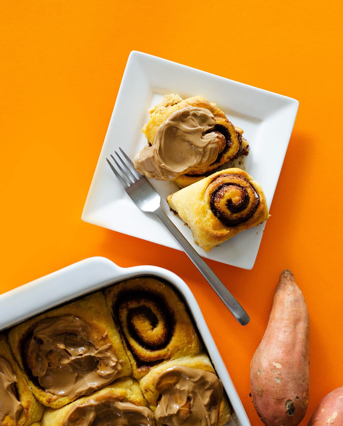 Cinnamon rolls on a plate with a fork - Fluffy, decadent, in slathered in a simple brown sugar cream cheese frosting, these Sweet Potato Cinnamon Rolls are the perfect way to wake up.