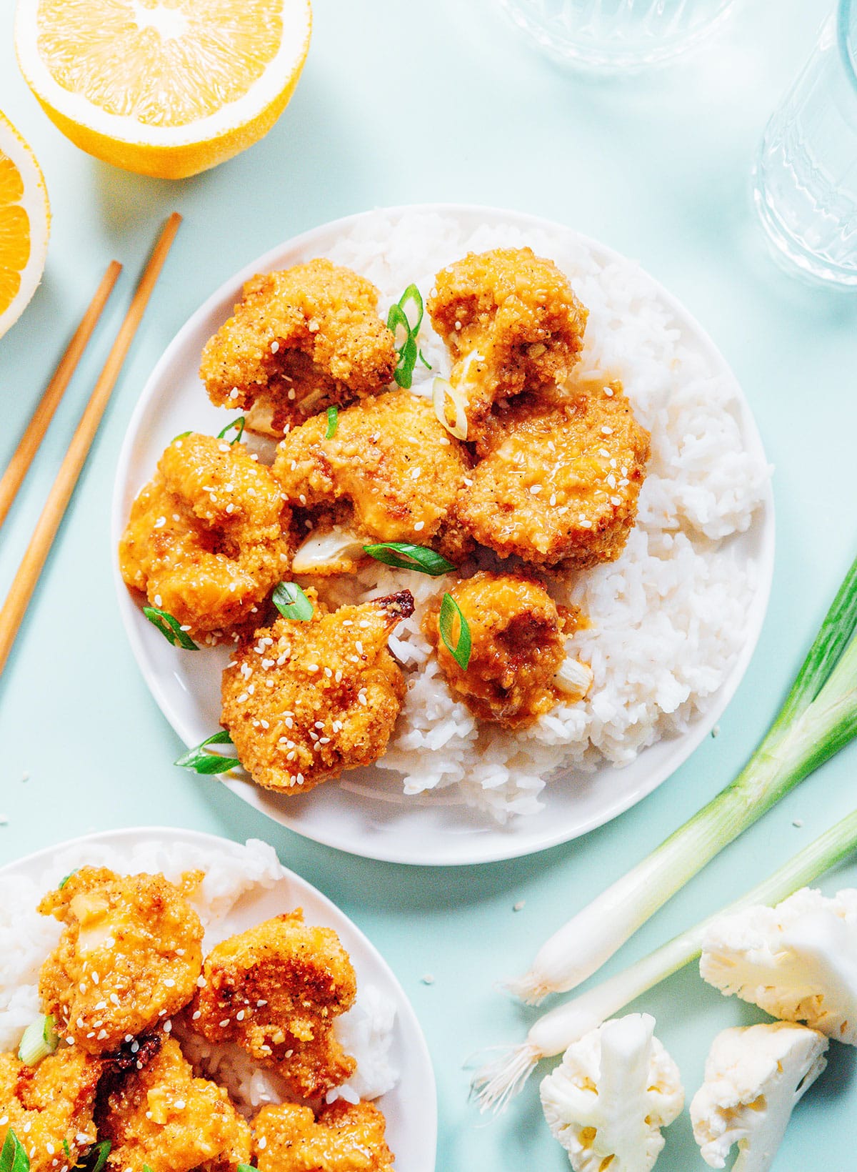 Sticky orange cauliflower with chives and sesame seeds on top of white rice.