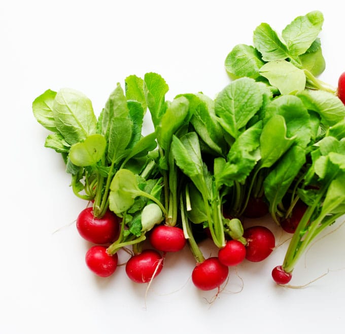 red radishes on a white background - These radish recipes are simple and delicious (and best of all, they'll make you actually WANT to eat your veggies!) Give them a try for a colorfully peppery crunch.