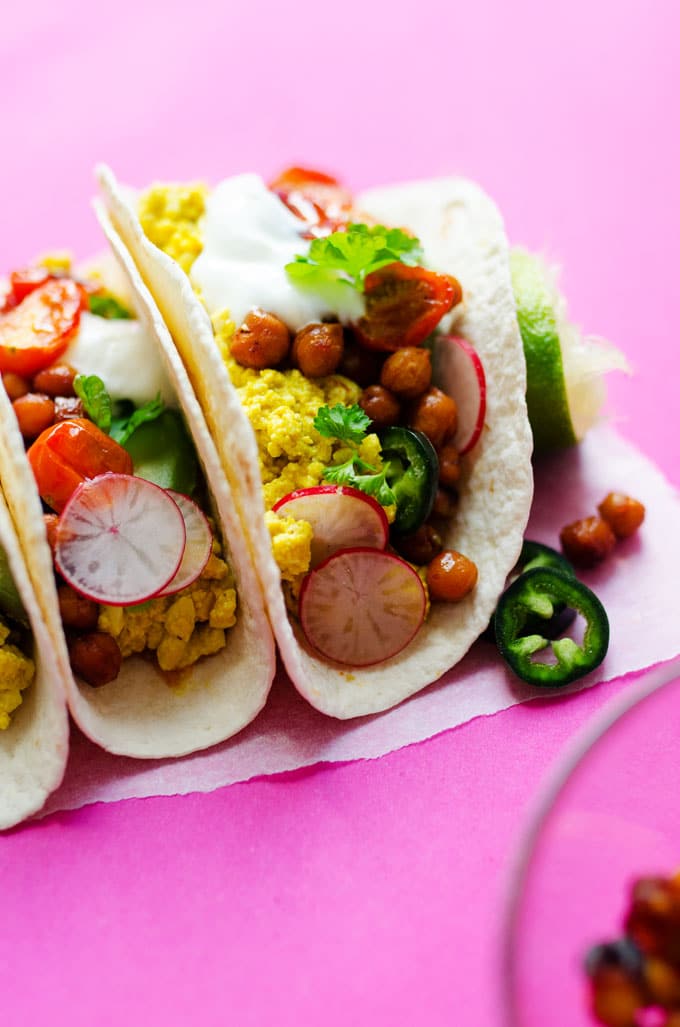 Vegan tofu scramble tacos on a pink background - These Vegan Breakfast Tacos are stuffed with flavorful tofu scramble, "bacon-y" crispy chickpeas, and smoky roasted tomatoes (all in under 30 minutes!)