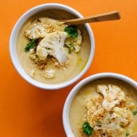 Cauliflower soup in a white bowl on orange background - Healthy Cauliflower Soup that's ultra-creamy AND easy AND vegan? It's happening and it is so much tastier that you can imagine.