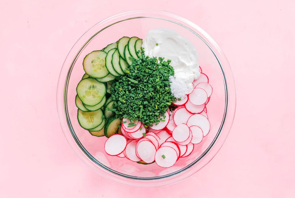 A clear glass bowl filled with unmixed spring radish salad ingredients