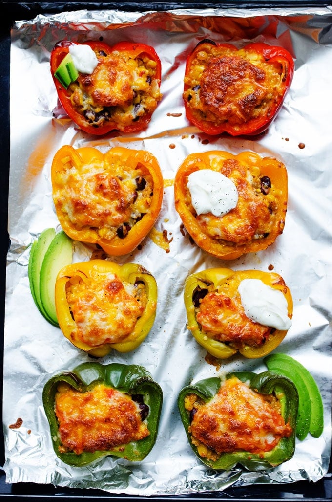 Quinoa stuffed peppers on a baking sheet with melted cheese, sour cream, and avocado.