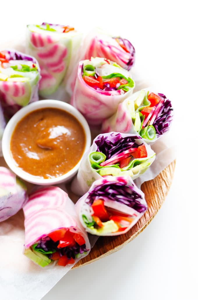Spring rolls with heart shaped beets on a white plate with almond butter dipping sauce - Stuffed with fuchsia root vegetables, creamy avocado, and herbs then served with the most delicious almond butter sauce of your life, these vegan spring rolls are perfect for your healthy Valentine's Day dinner.