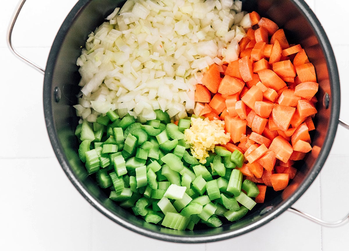 A pot filled with chopped onion, carrots, celery, and garlic