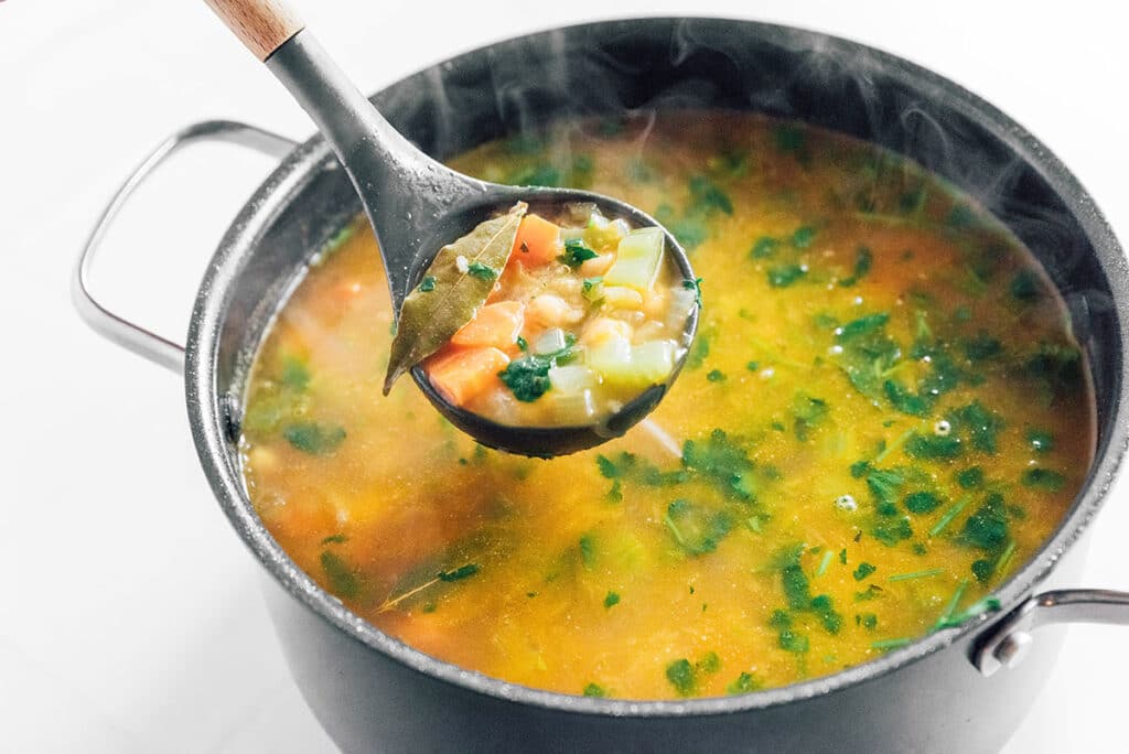 A ladle scooping a spoonful of quinoa vegetable soup from a large pot