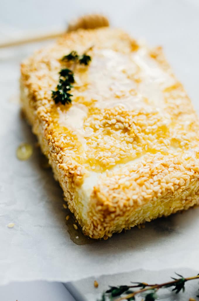 Baked feta on a marble white background with thyme - This Sesame Crusted Baked Feta is easy to make and is the prefect appetizer with some pita chips and fresh veggies.