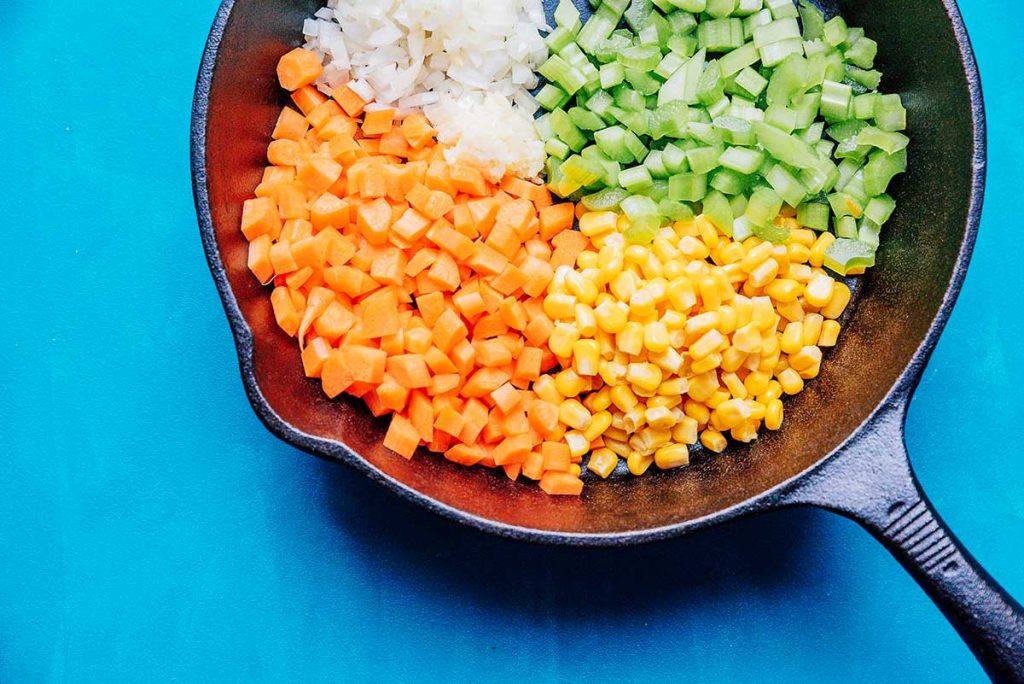 Carrots, corn, celery, and onion in a cast iron skillet with a blue background