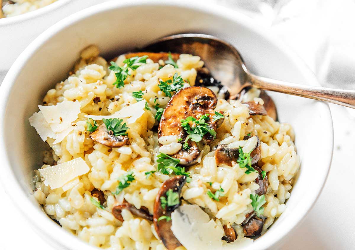 A white bowl filled with mushroom risotto and topped with parmesan flakes.