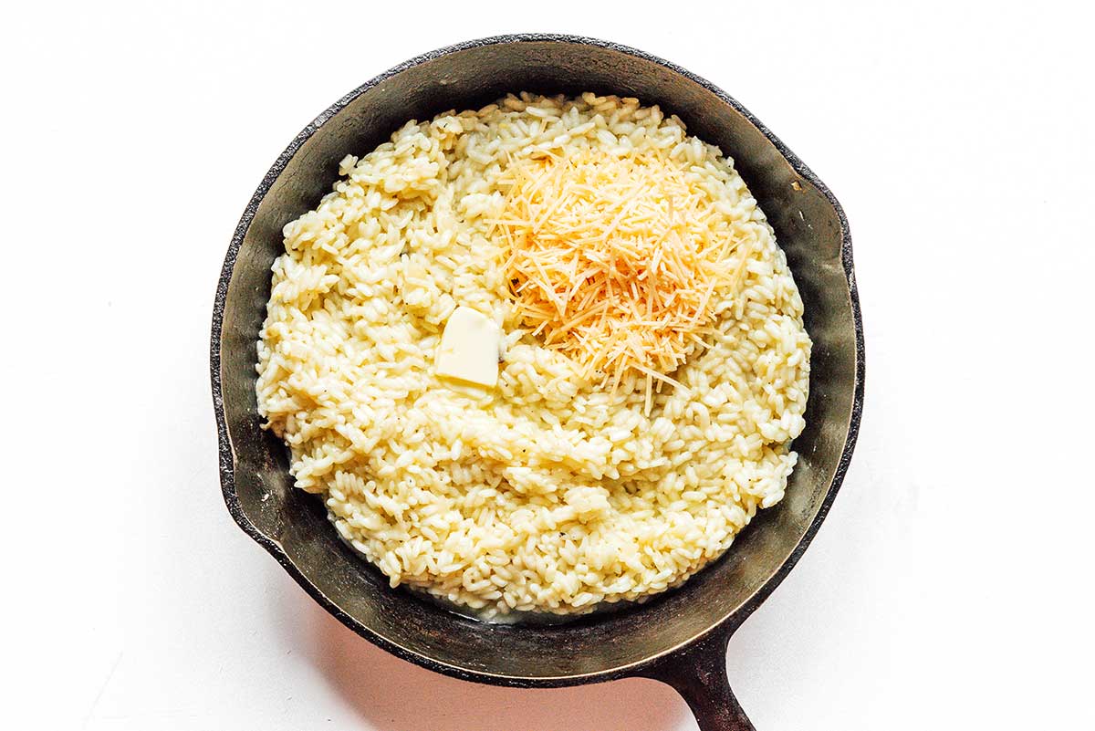 A cast iron skillet filled with cooked, fluffy risotto and topped with cheese and butter.
