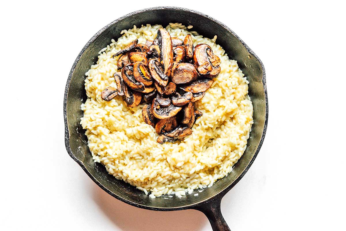 A cast iron skillet filled with cooked, fluffy risotto and topped with cooked mushroom slices.