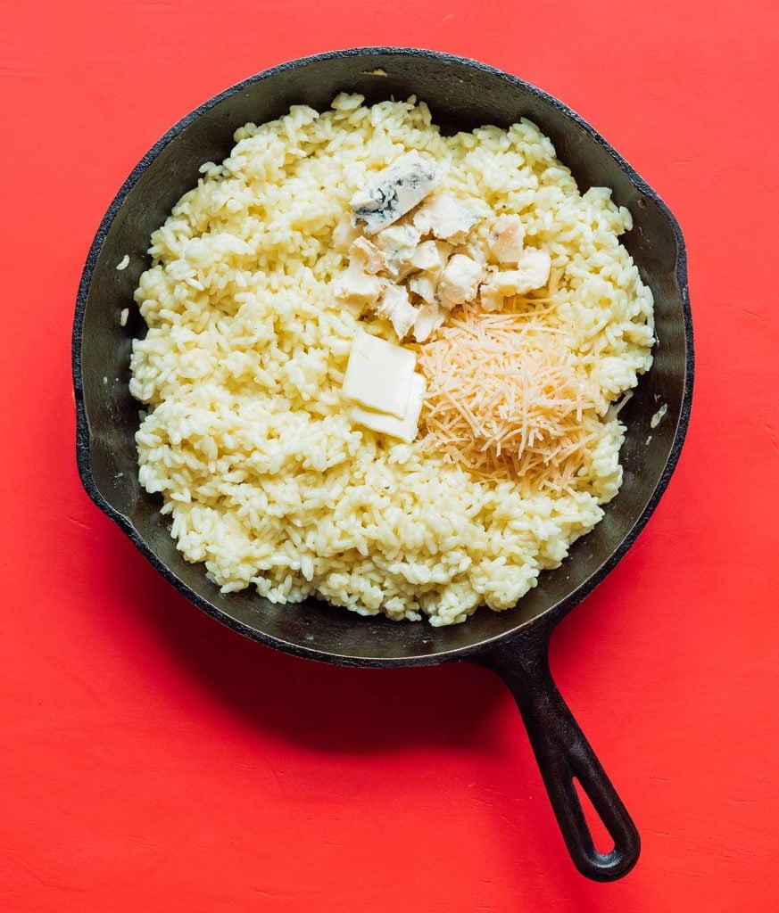 A cast iron skillet filled with Arborio rice and topped with butter, gorgonzola, and parmesan