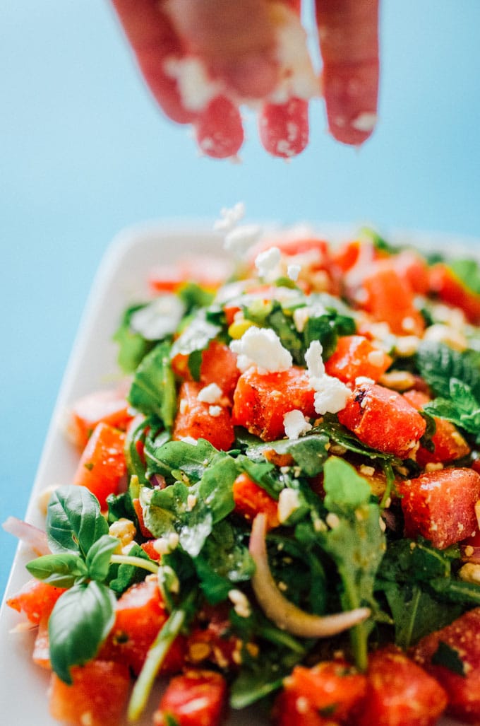 Grilled watermelon salad with arugula, feta cheese, and mint in a bowl on a blue background
