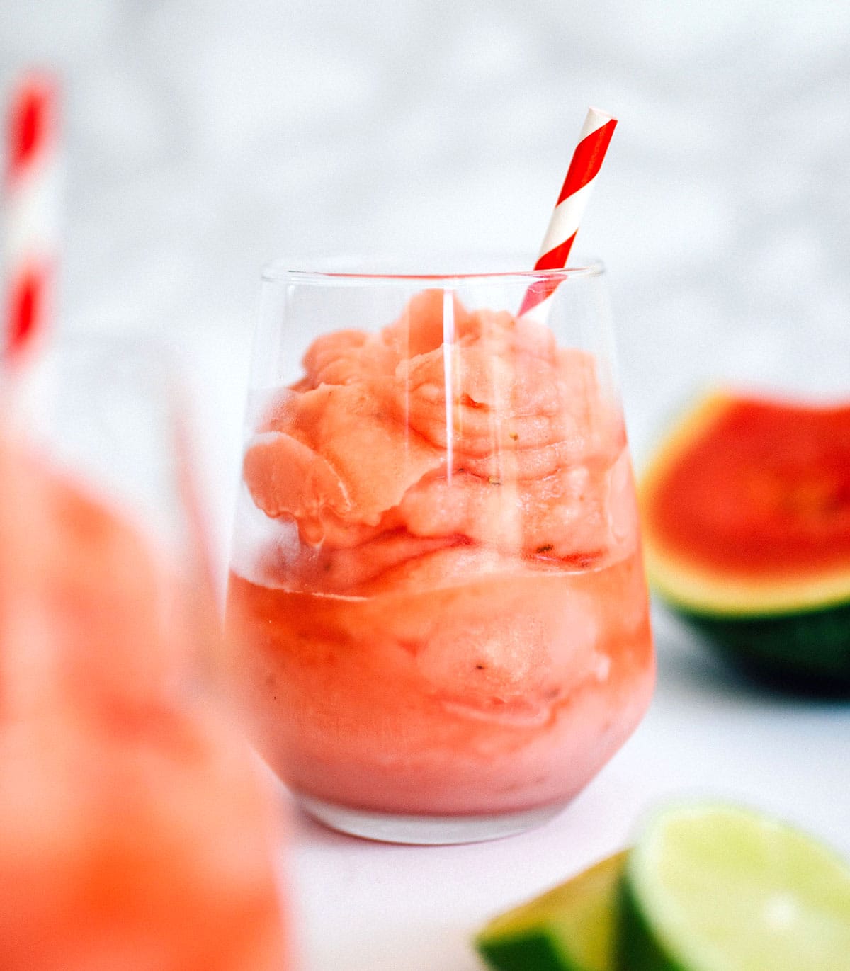 Watermelon daiquiri in a glass with a red and white straw and watermelon and lime slices on the side.