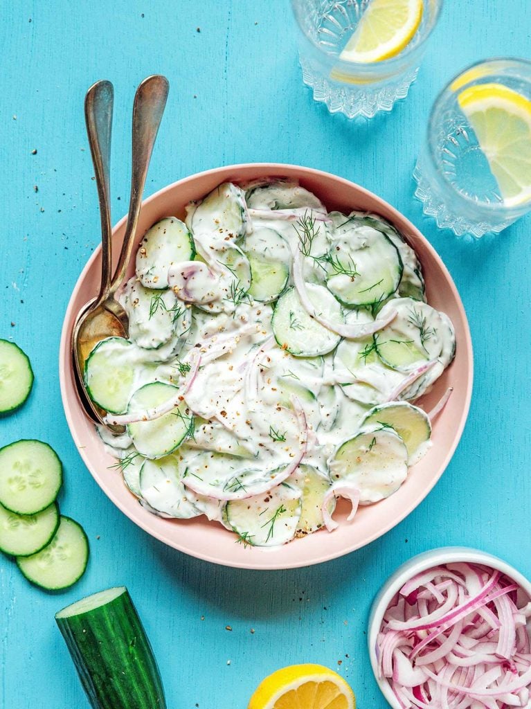 A large pink bowl filled with creamy cucumber salad