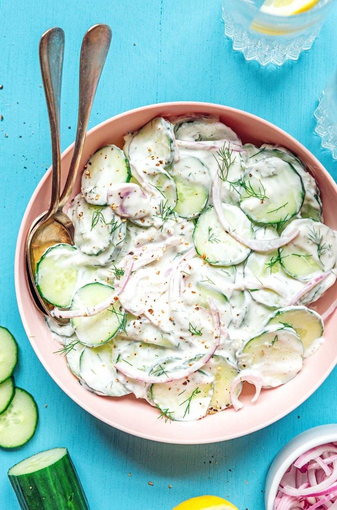 A large pink bowl filled with creamy cucumber salad
