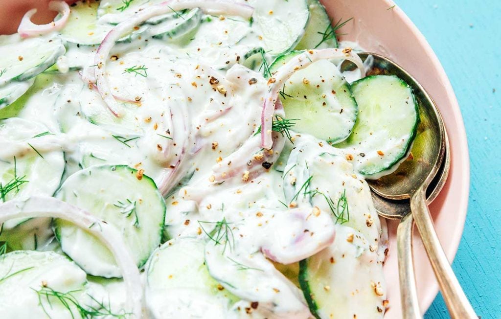 A close of view of a large pink bowl filled with creamy cucumber salad