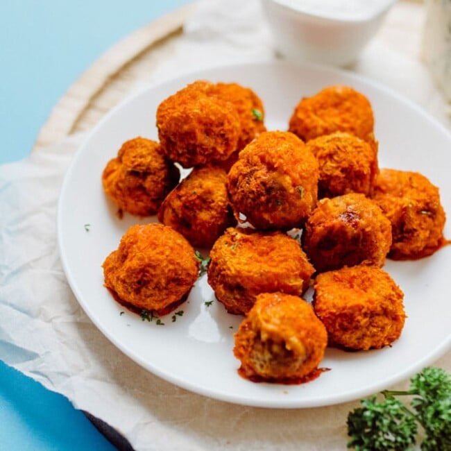 Buffalo mushroom poppers on a white plate with a blue background - These Buffalo Mushroom Poppers are stuffed with creamy jalapeno filling, coated in a quick panko crust, baked to crispy perfection, and topped off with buffalo sauce and bleu cheese dipping sauce. 