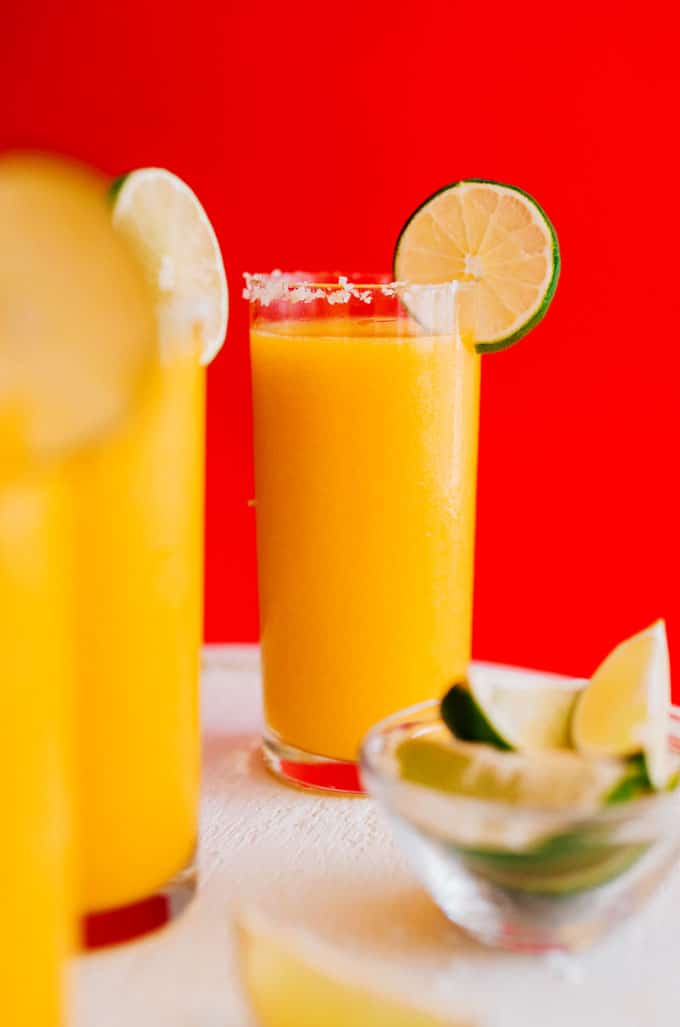 Frozen mango margarita slush in a glass with a slice of lime on a red background