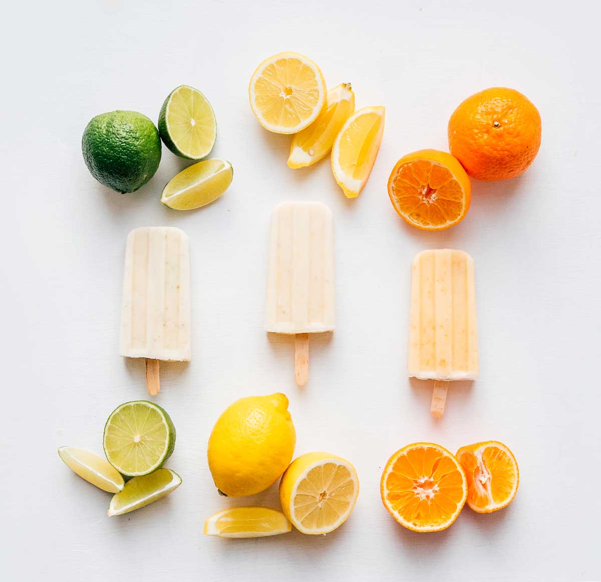 Lime, lemon, and orange creamsicle popsicles on a white background with citrus fruit
