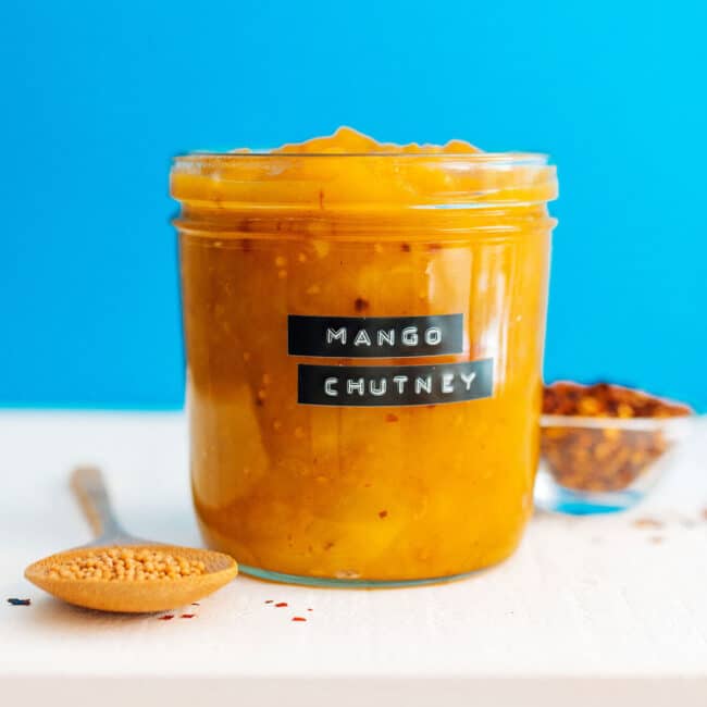 Labeled jar of mango chutney on a blue background.