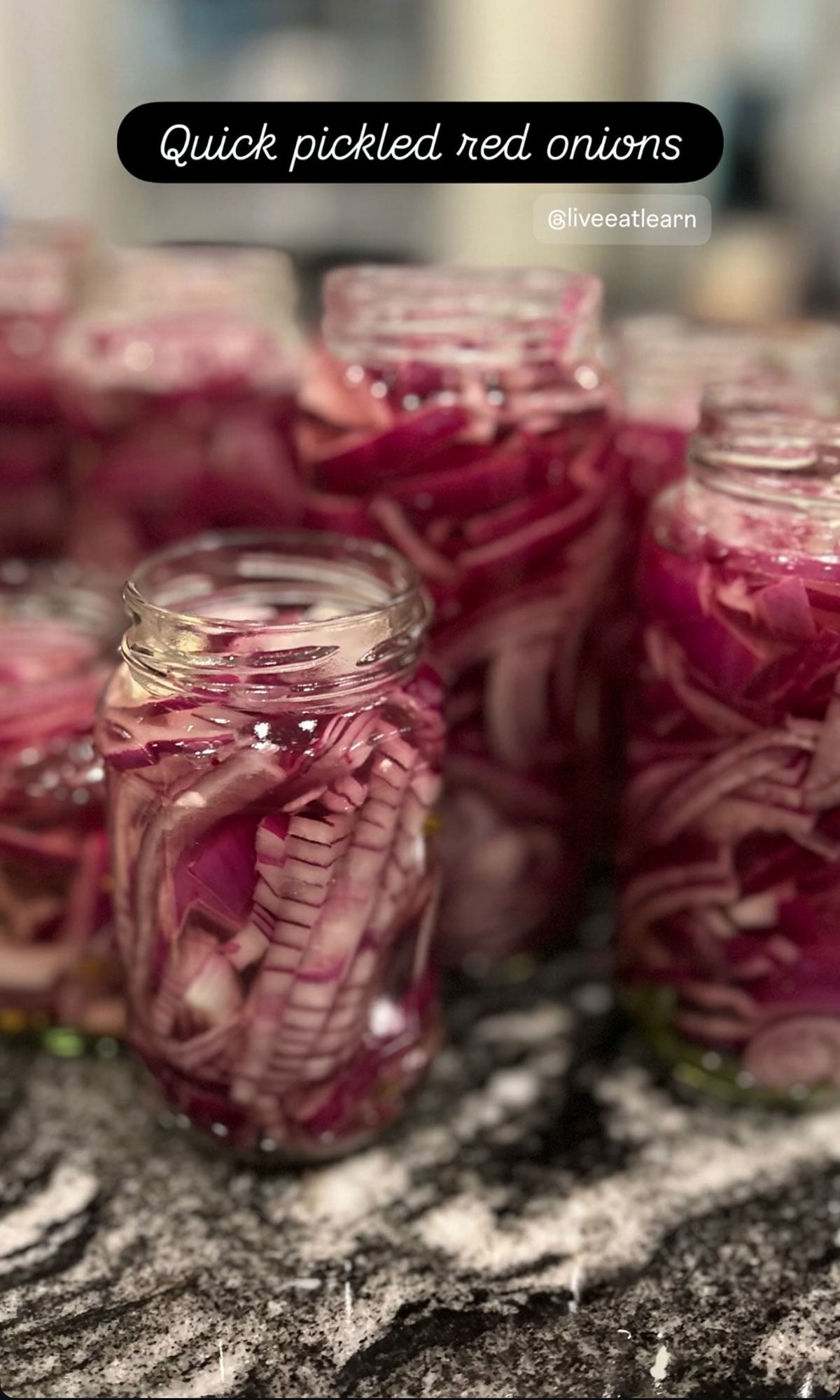 Multiple glass jars filled with sliced red onions and pickled red cabbage are arranged on a countertop. Text reads “Quick pickled red onions.”.
