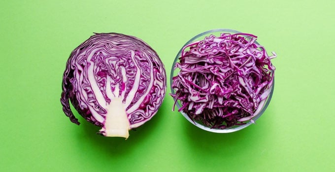 Half a head of red cabbage with a bowl of shredded cabbage on a green background