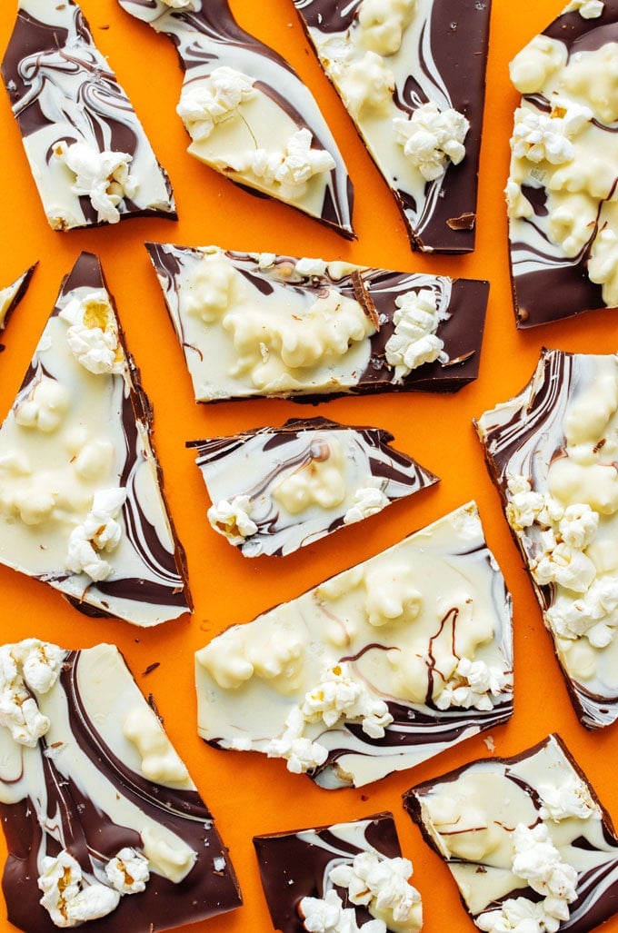 Pieces of swirled dark and white chocolate bark with salted popcorn on an orange background