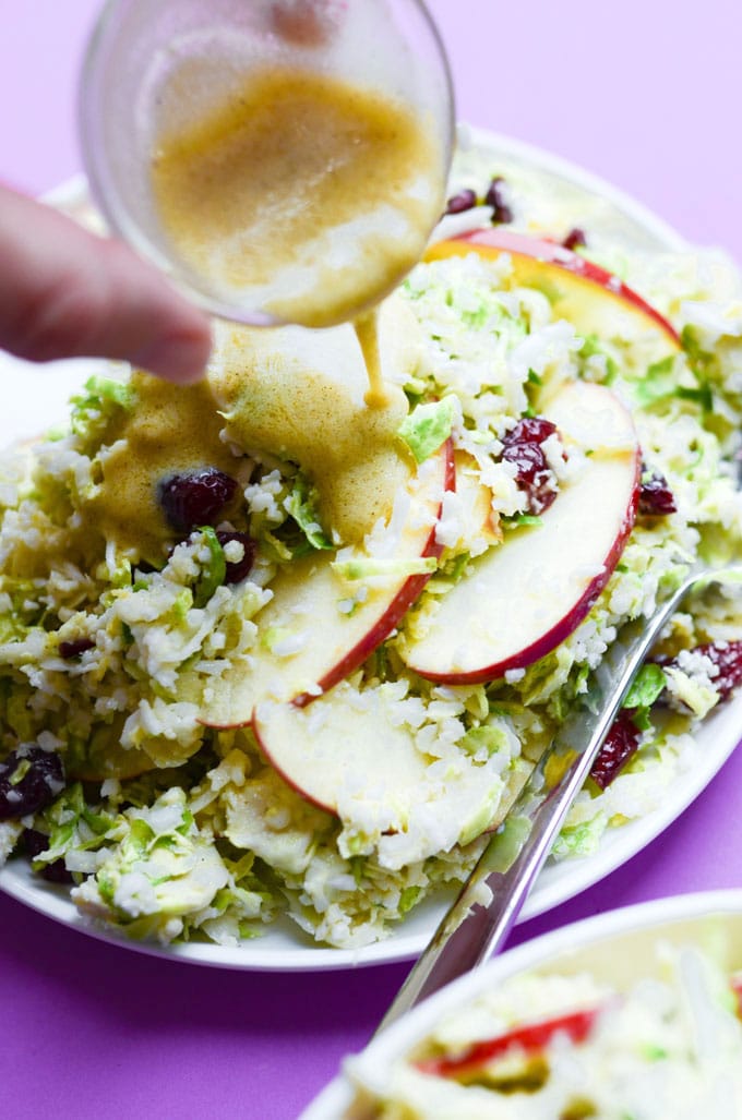 Pouring honey mustard dressing onto shaved Brussels sprout salad with apples