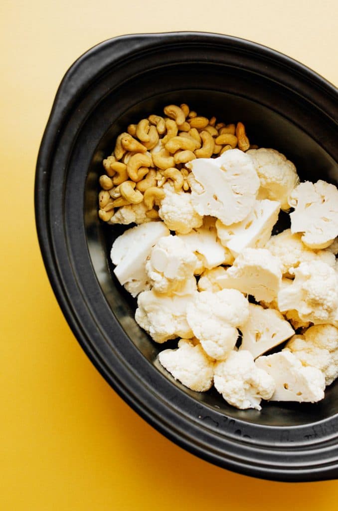 Cauliflower and cashews in a slow cooker with a yellow background