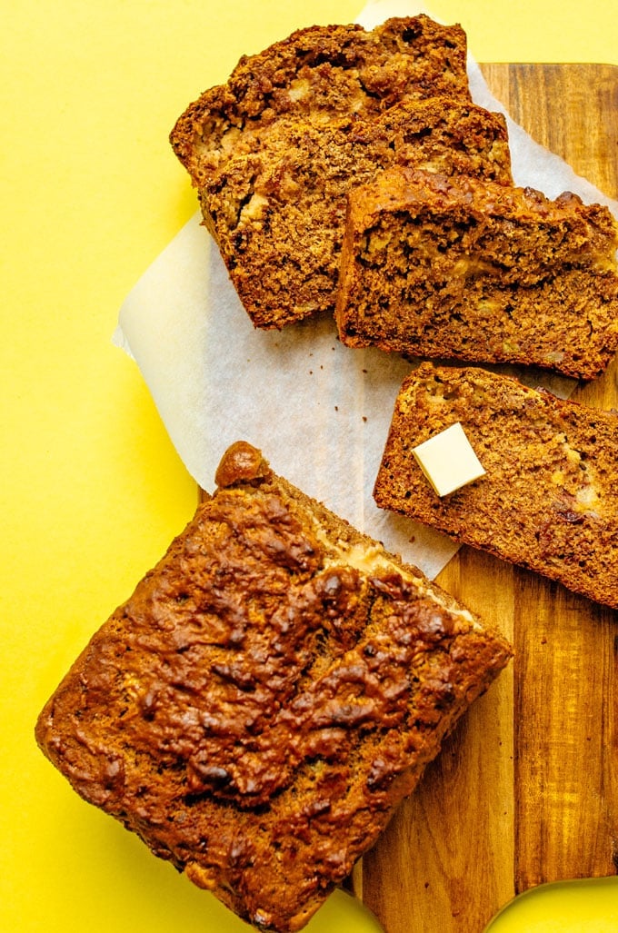 Banana bread slices on a wooden cutting board with yellow background
