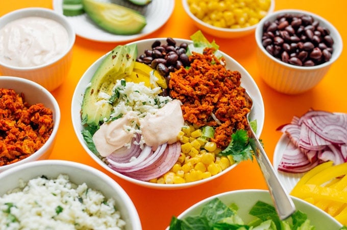 Burrito bowl with tempeh and vegetables on an orange background