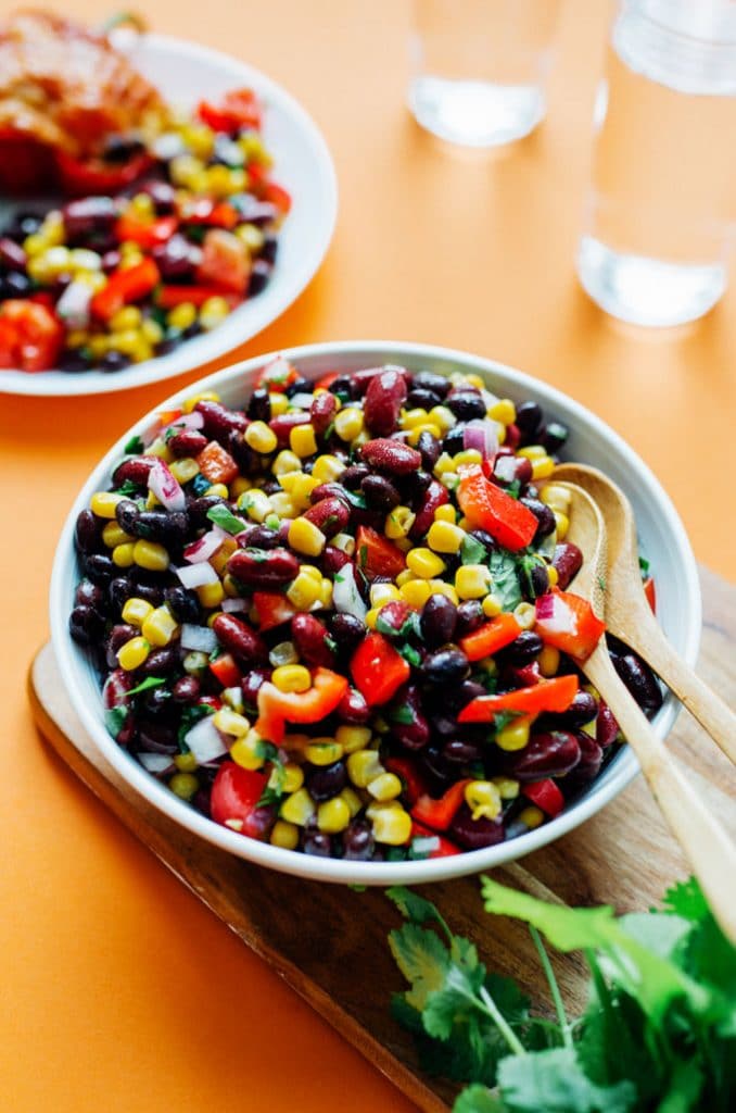 Bean salad in a glass bowl on orange background - This easy Bean Salad recipe is famous in our house, and for good reason! Quick to make, packed with flavor, and perfect for bringing to potlucks!