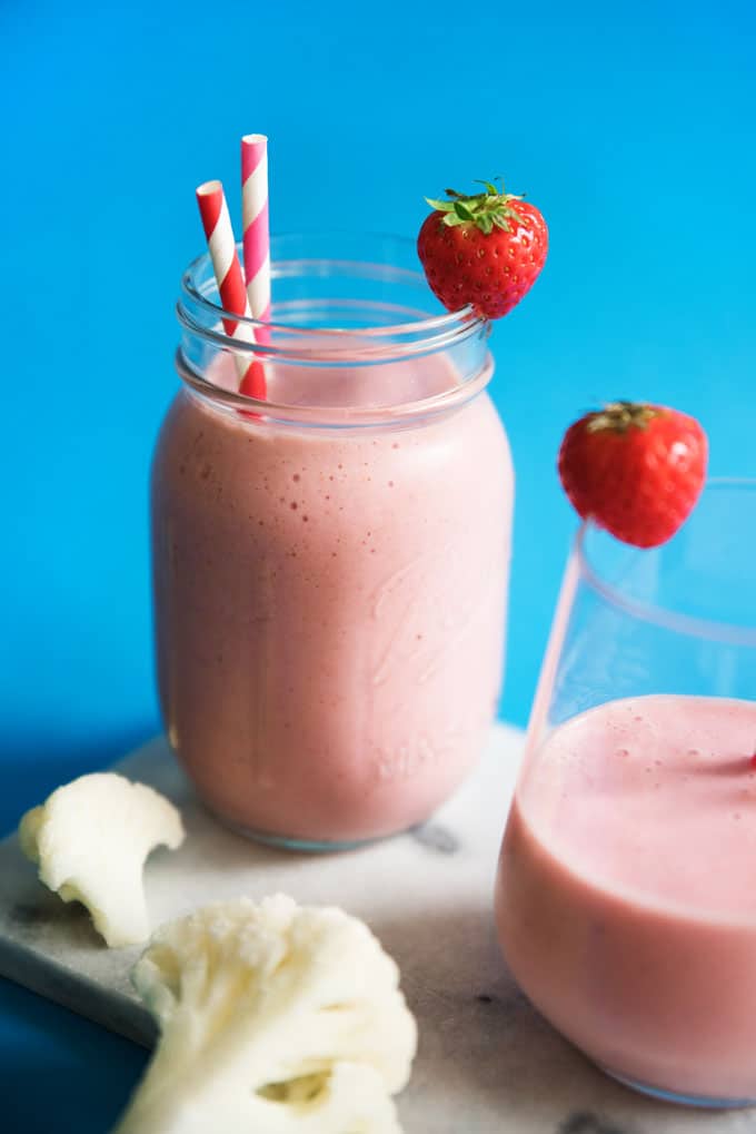 Hidden cauliflower smoothie with strawberry and paper straws in a glass on a blue background