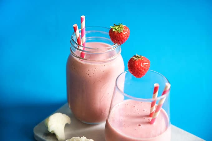 Hidden cauliflower smoothie with strawberry and paper straws in a glass on a blue background