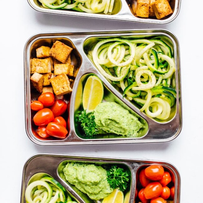 Meal prep container with zucchini noodles on white background - This Zucchini Noodles Vegetarian Meal Prep is a low carb lunch solution that will have you looking forward to lunchtime! Packed with fresh veggies, avocado pesto, and crispy baked tofu.