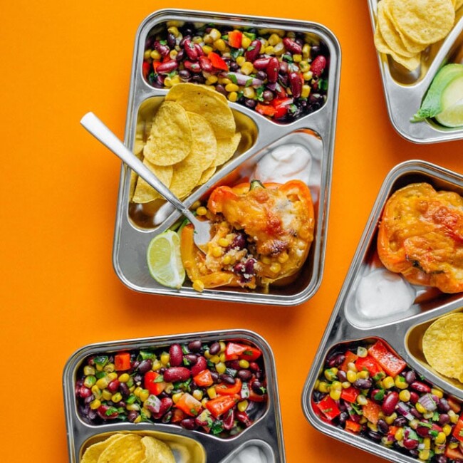 Meal prep containers with bean salad and stuffed peppers on an orange background