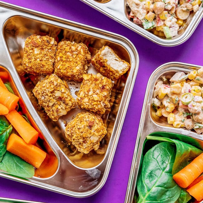 Meal prep boxes on purple background - Vegetarian meal prep that's sure to keep you full all day. Almond crusted tofu nuggets paired with a creamy, veggie-packed chickpea corn salad!