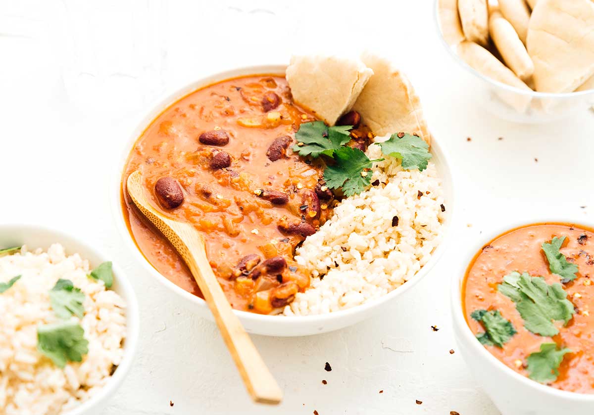 A bowl of coconut kidney bean curry, rice, and bread surrounded by bowls filled with various ingredients