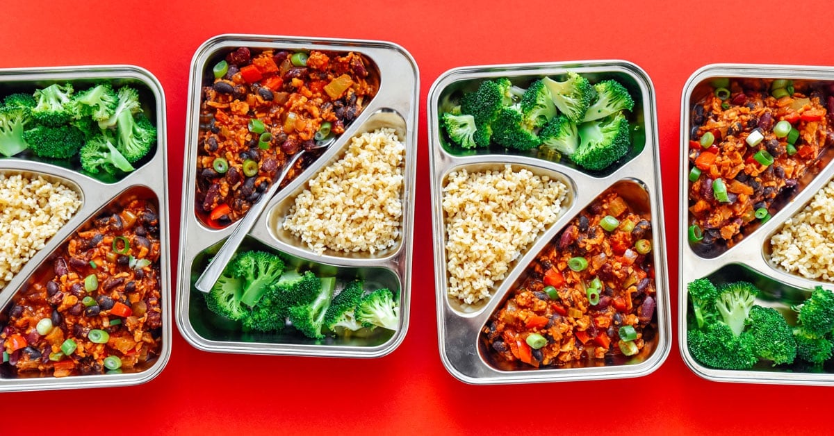 Meal prep containers with broccoli, chili, and bulgur on a red background - This vegan Tempeh Chili Meal Prep is ready in 30 minutes and takes care of lunch for the week (plus it's like...really tasty).
