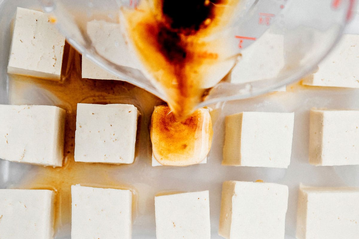 Pouring marinade over pieces of tofu.