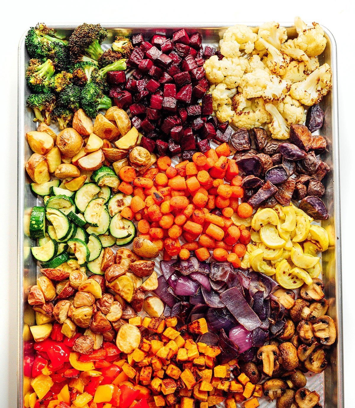 Many colorful veggies on a baking sheet next to an air fryer.