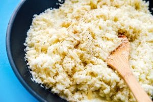 Cauliflower risotto recipe in a bowl on a blue background - This Cauliflower Risotto recipe is a low carb, keto-friendly twist on traditional risotto. Creamy and cheesy, without all the carbs!