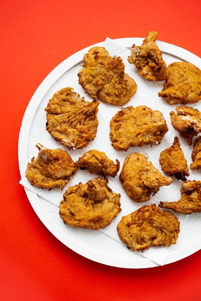 Air fryer fried oyster mushrooms recipe that tastes like vegetarian fried chicken in a bowl on a red background.