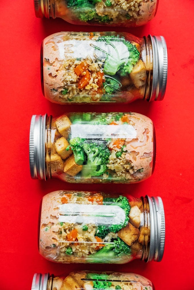 Vegetarian stir fry meal prep idea in mason jars on a red background