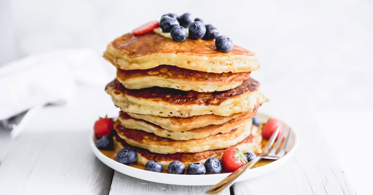 Stack of the best buttermilk pancakes with berries on a white background.